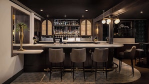 A bar area with a counter, stools, and a well-stocked shelf. - Wylie Hotel Atlanta, Tapestry Collection by Hilton (Atlanta)