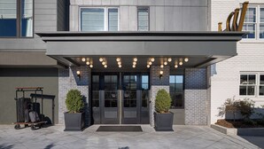 A modern building entrance with a double door, a covered entrance area, and a luggage cart. - Wylie Hotel Atlanta, Tapestry Collection by Hilton (Atlanta)