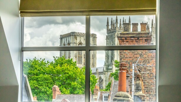 A window with a view of a historic building with multiple spires and a brick chimney. - 7 Aspire -  a family break that sleeps 4 guests  in 2 bedrooms (York)
