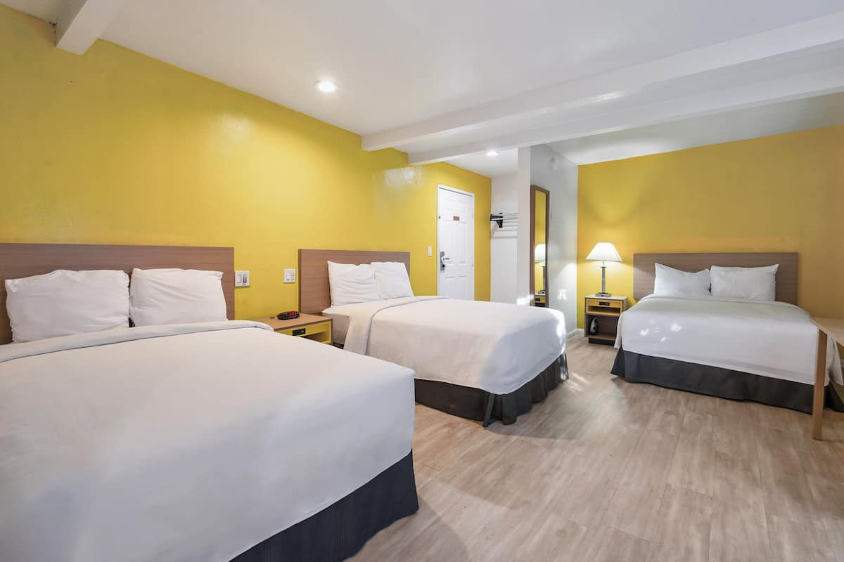 A hotel room with two beds, a wooden floor, and a yellow wall.