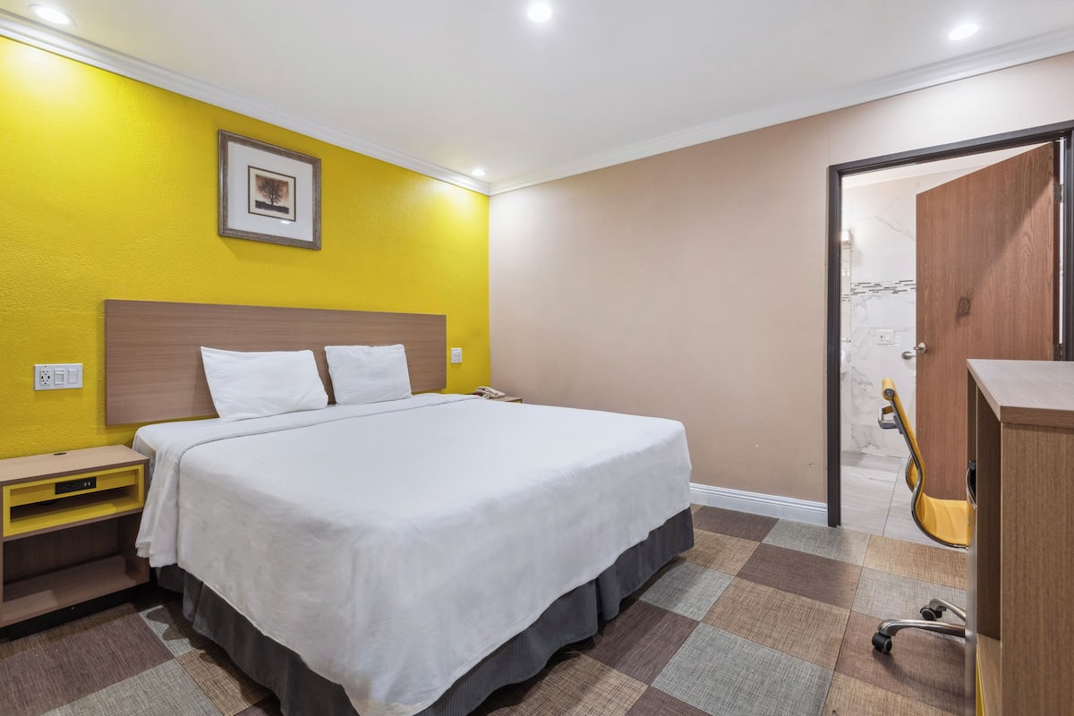 A hotel room with a bed, a nightstand, a desk, and a chair.