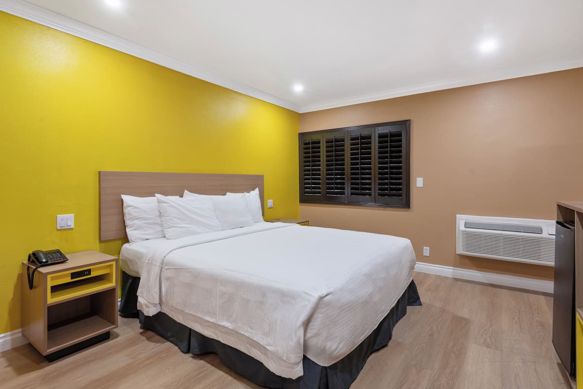 A neatly arranged hotel room with a bed, bedside table, and a wall-mounted air conditioning unit.