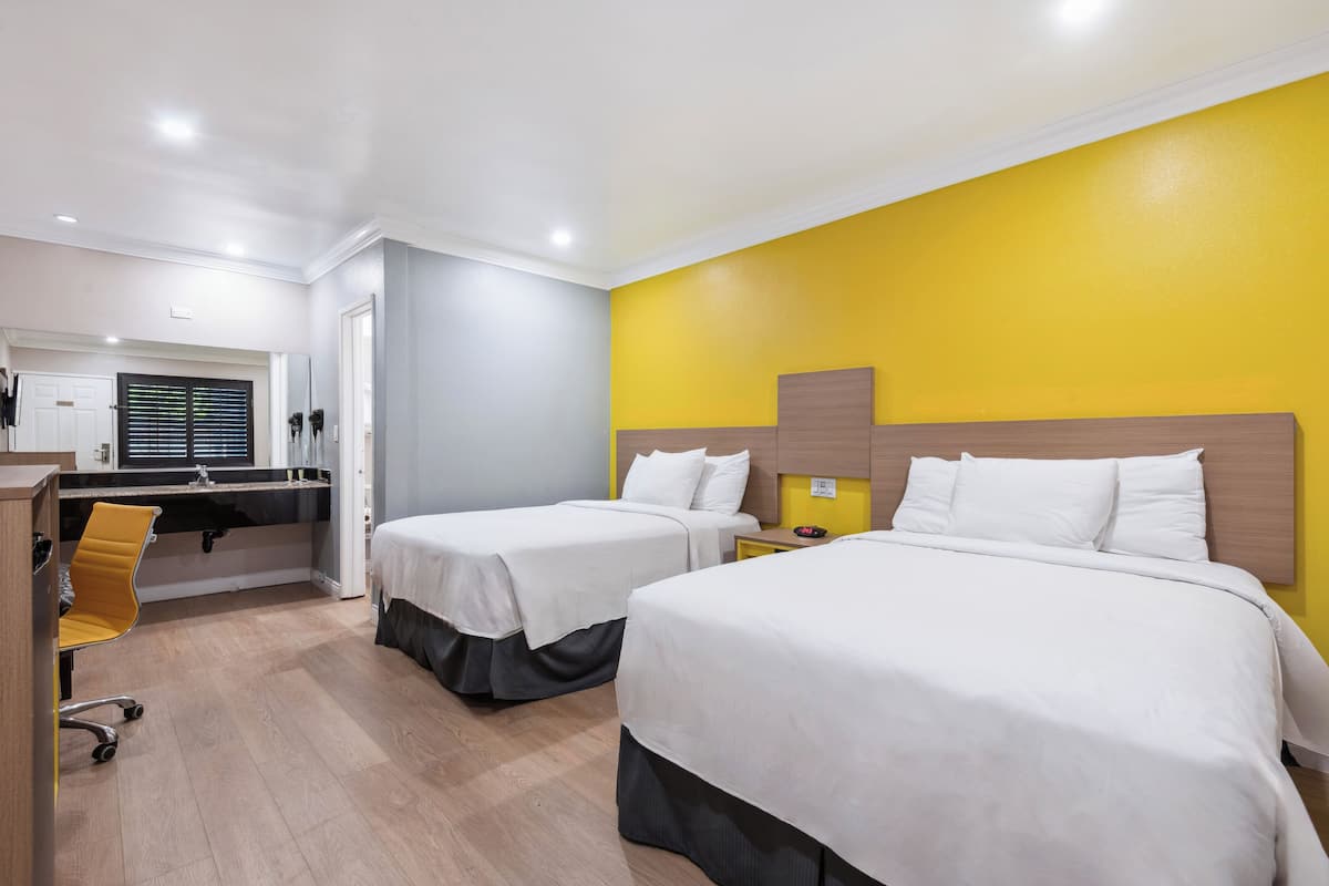 A hotel room with two beds, a desk, and a chair.