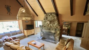 Ein gemütliches Wohnzimmer mit Kamin aus Stein, Holzmöbeln und einem Fernseher auf einem Holzkasten.