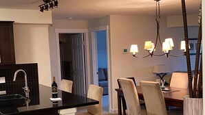A modern kitchen with a black countertop, a wine bottle, and a dining area with a chandelier. - Top floor condo on Lake Windermere with spectacular lake and Mountain View’s (Invermere)