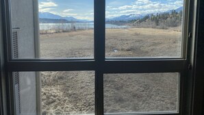 A window with a view of a dry field, mountains, and a lake. - Top floor condo on Lake Windermere with spectacular lake and Mountain View’s (Invermere)