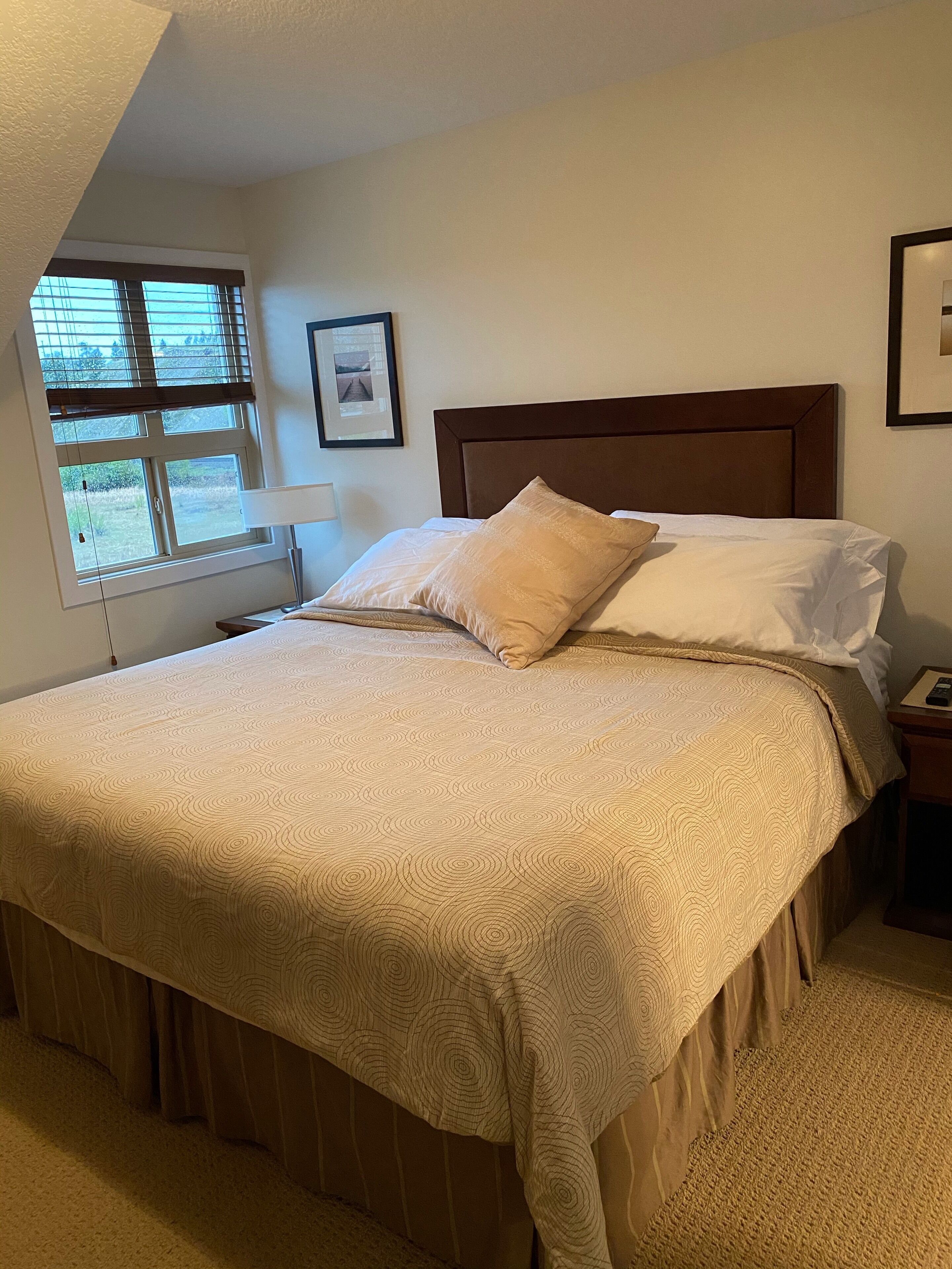A neatly made bed with a patterned bedspread, a wooden headboard, and a bedside table with a lamp.