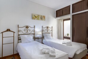 A hotel room with two beds, a wardrobe, a window with curtains, and a wall-mounted artwork.