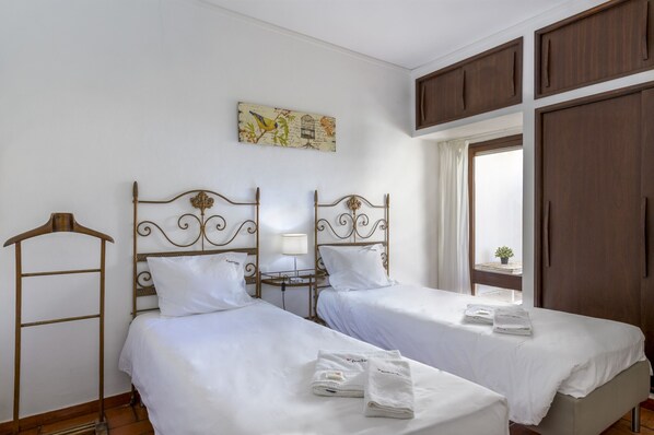 A hotel room with two beds, a wardrobe, a window with curtains, and a wall-mounted artwork.