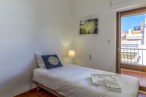 A neatly made bed with white linens and a blue decorative pillow, a bedside lamp, and a painting on the wall.