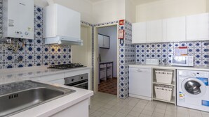 Cocina compacta con estufa a gas, muebles blancos, lavadora y azulejos de salpicadero con diseño.