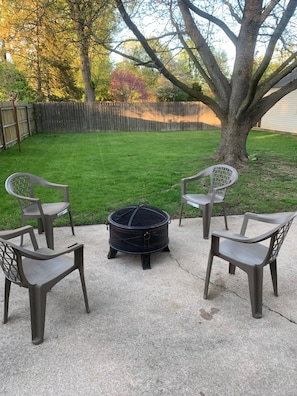 Relax by the fire pit in a serene outdoor space surrounded by a lush lawn and a wooden fence.