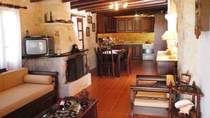Un saló acollidor amb un sofà, una taula de centre amb ampolles, una televisió i una llar de foc. Hi ha una zona de cuina amb un taulell i un rentaplat.