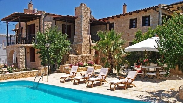 Zona de piscina amb gandules i un edifici de pedra al fons.