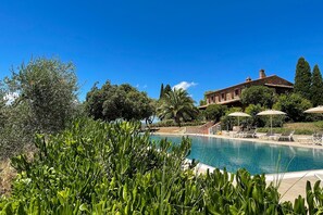 A pool area with lounge chairs and umbrellas, surrounded by greenery and a stone building in the background. - Villa Campo Valerio with large Swimming Pool (Scarlino)