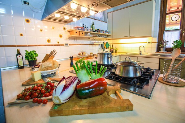 A kitchen with a stove, pots, a cutting board with vegetables, and a sink. - Villa Campo Valerio with large Swimming Pool (Scarlino)