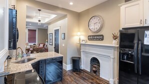 A kitchen with a granite countertop, stainless steel appliances, a white fireplace, and a clock on the wall.