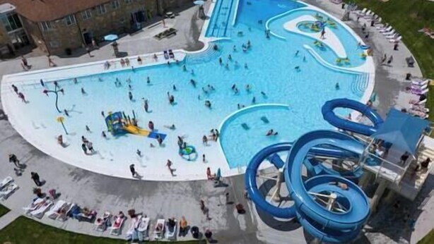An aerial view of a water park with multiple swimming pools, slides, and a large blue spiral water feature.