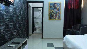 A hotel room with a bed, a TV, a bathroom, and a painting on the wall. - Room-ambience Hotel Magodo - Guest Room (Lagos)