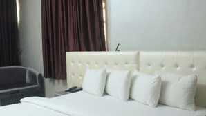 A hotel room with a large bed, a chair, and a nightstand. - Room-ambience Hotel Magodo - Guest Room (Lagos)