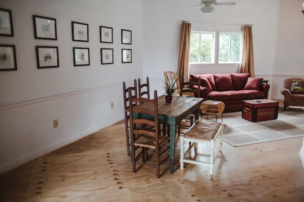 A dining area with a wooden table and chairs, a red sofa, and a window with curtains.