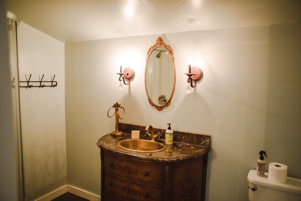 Une salle de bain avec un meuble-lavabo en bois, un lavabo doré, un grand miroir et des toilettes.