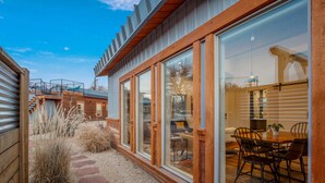 A modern house with large glass windows, a wooden deck, and a dining area with chairs and a table. - Luxe stay in Kanab with stargazing rooftop deck, pool & hot tub (Kanab)