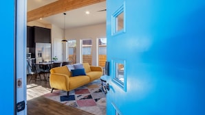 A modern living room with a yellow sofa, a blue door, and a kitchen in the background. - Luxe stay in Kanab with stargazing rooftop deck, pool & hot tub (Kanab)