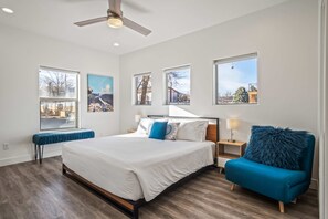 Ein modernes Schlafzimmer mit einem großen Bett, einem blauen Sessel und mehreren Fenstern mit Blick ins Freie.