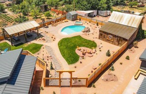 Ein Garten mit Swimmingpool, überdachter Terrasse und einem eingezäunten Bereich mit Liegestühlen.