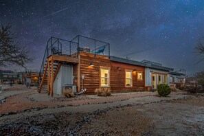 Une cabane moderne en bois, dotée d’un balcon, de grandes fenêtres et offrant une vue dégagée sur le ciel nocturne.