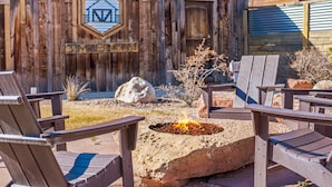 Een houten terras met Adirondack stoelen, een vuurkorf met vuur, en een houten wand met een logo en de tekst 