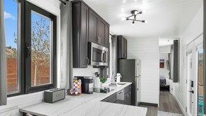 A modern kitchen with dark cabinets, a marble countertop, and a built-in microwave.