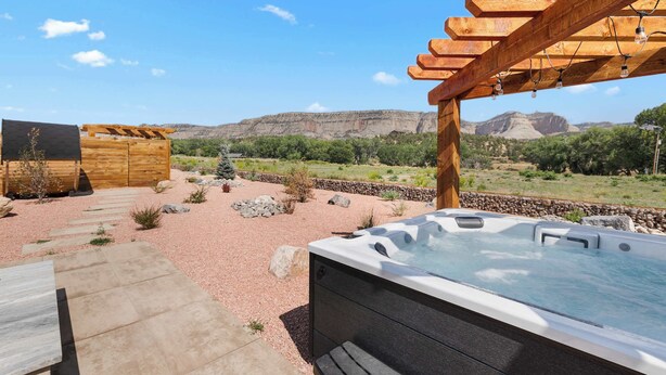 A hot tub with a view of a mountainous landscape, a wooden pergola, and a stone pathway. - Cozy Container Retreat near Zion Hot tub & Sauna (Orderville)