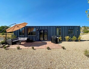 A modern container home with a patio, outdoor seating, and a covered area.