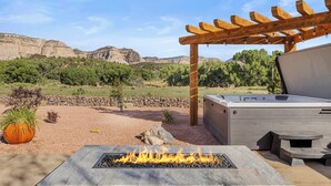 A fire pit with a stone surround, a pergola with lights, and a view of a mountainous landscape.