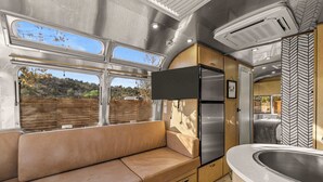 A compact kitchenette with a refrigerator, a sink, and a window overlooking a scenic landscape.