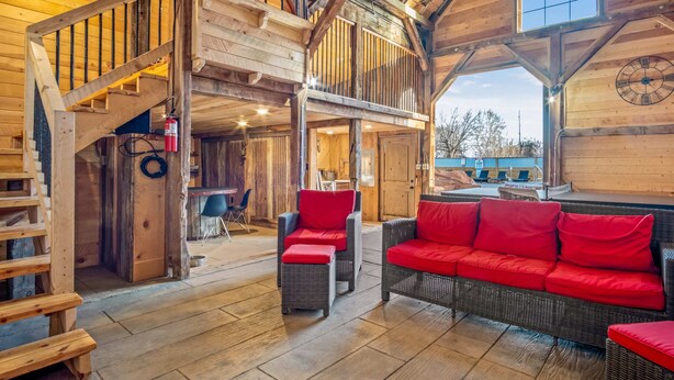 A spacious wooden interior with a high ceiling, a staircase leading to an upper level, and a cozy seating area with red cushions.