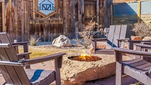 Una terraza de madera con sillas Adirondack, un pozo de fuego y una pared de madera rústica con un logotipo y un cartel con el nombre.