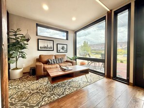 A living room with a brown leather sofa, a coffee table, a large potted plant, and two framed pictures on the wall. - East Zion Designer Container Studio- The Fields (Orderville)