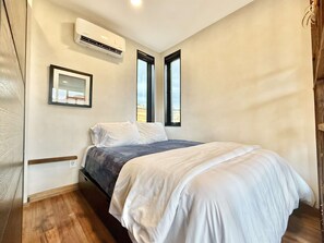 A bedroom with a bed, white walls, a window, and an air conditioning unit. - East Zion Designer Container Studio- The Fields (Orderville)
