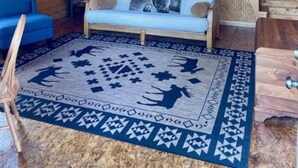 Een kamer in een chalet met een hoogslaper, een bank, een vloerkleed met dierenprint en houten wanden.