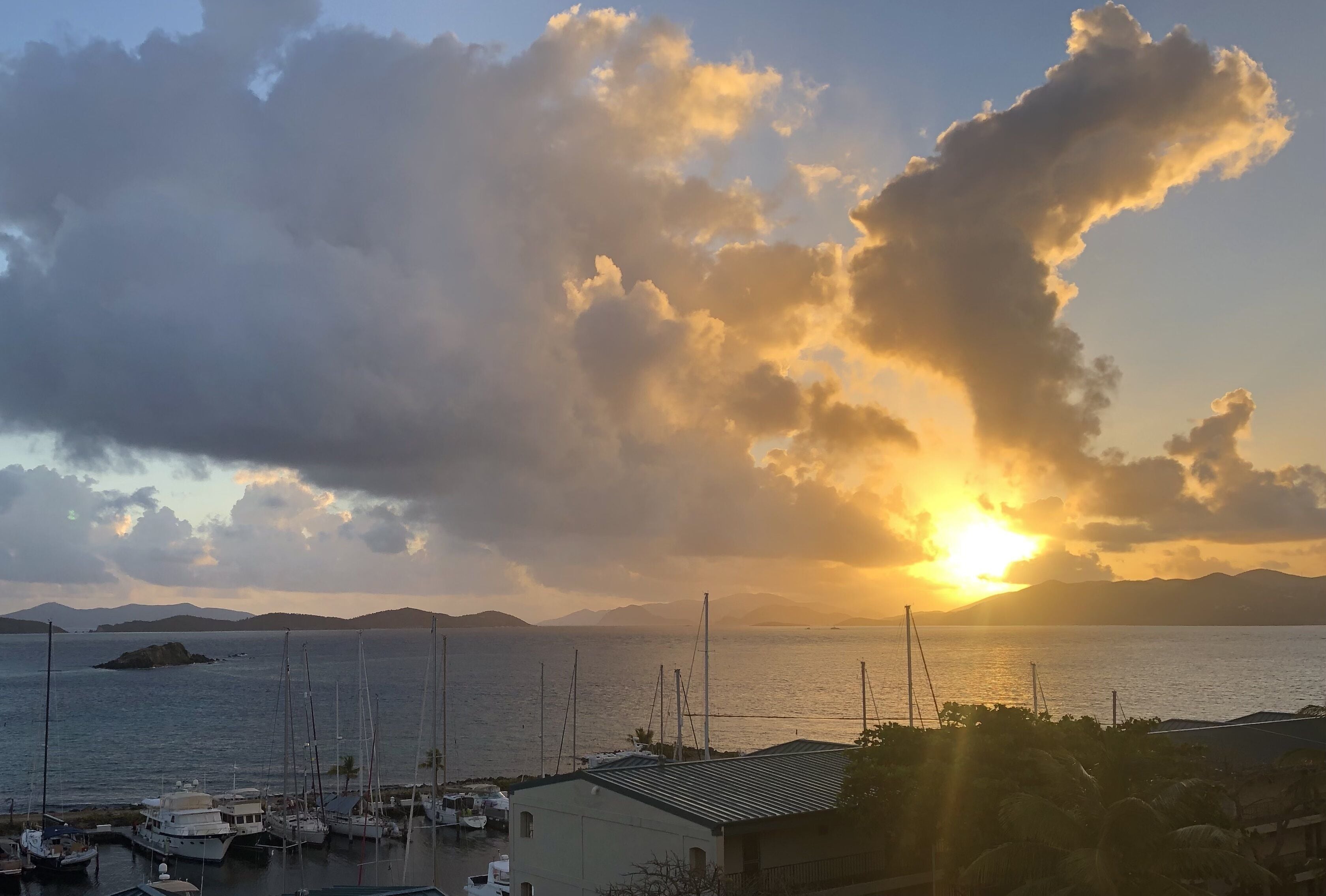 En lysthavn med fortøjede både, en bygning med sadeltag og solnedgang over vandet.