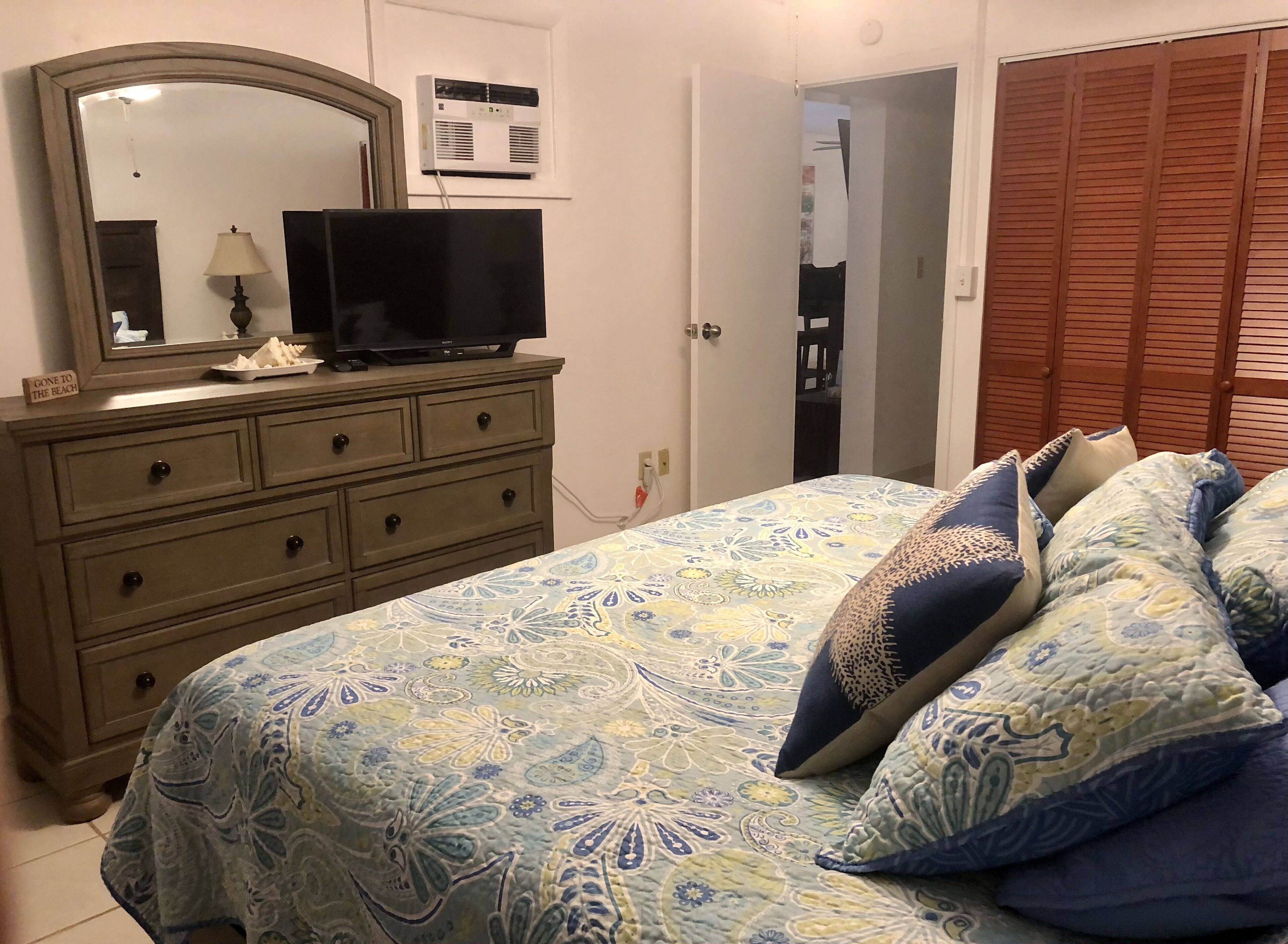 Un dormitorio con cama, cómoda, televisor y armario.