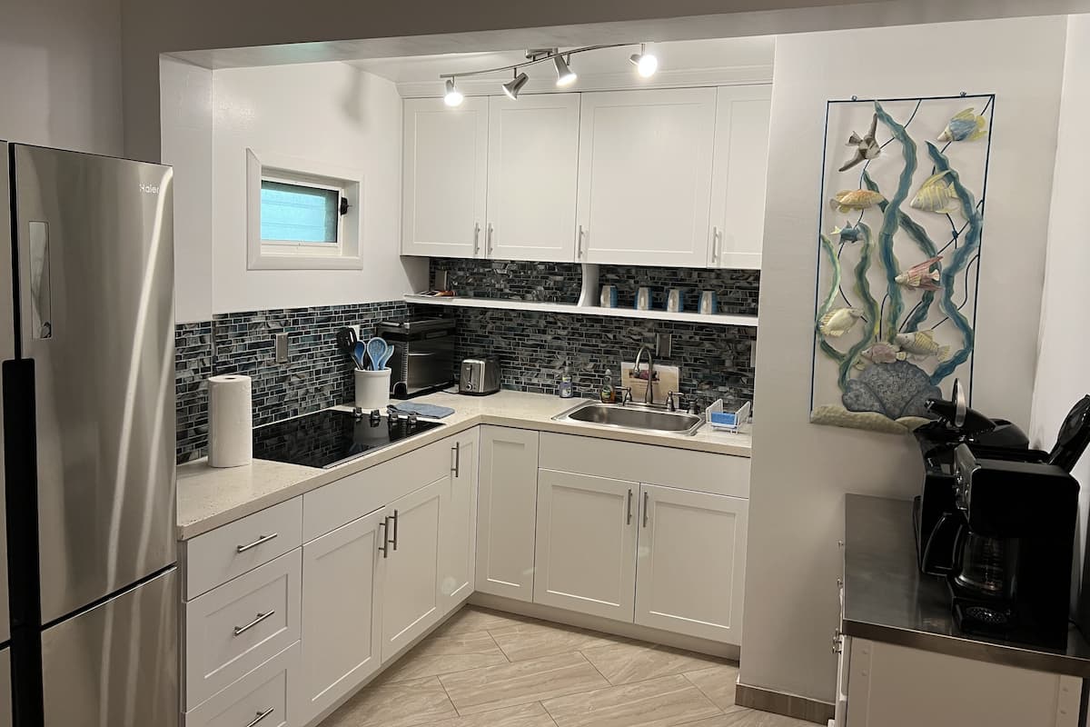 A modern kitchen with white cabinets, a stainless steel refrigerator, a black stove, and a coffee maker.