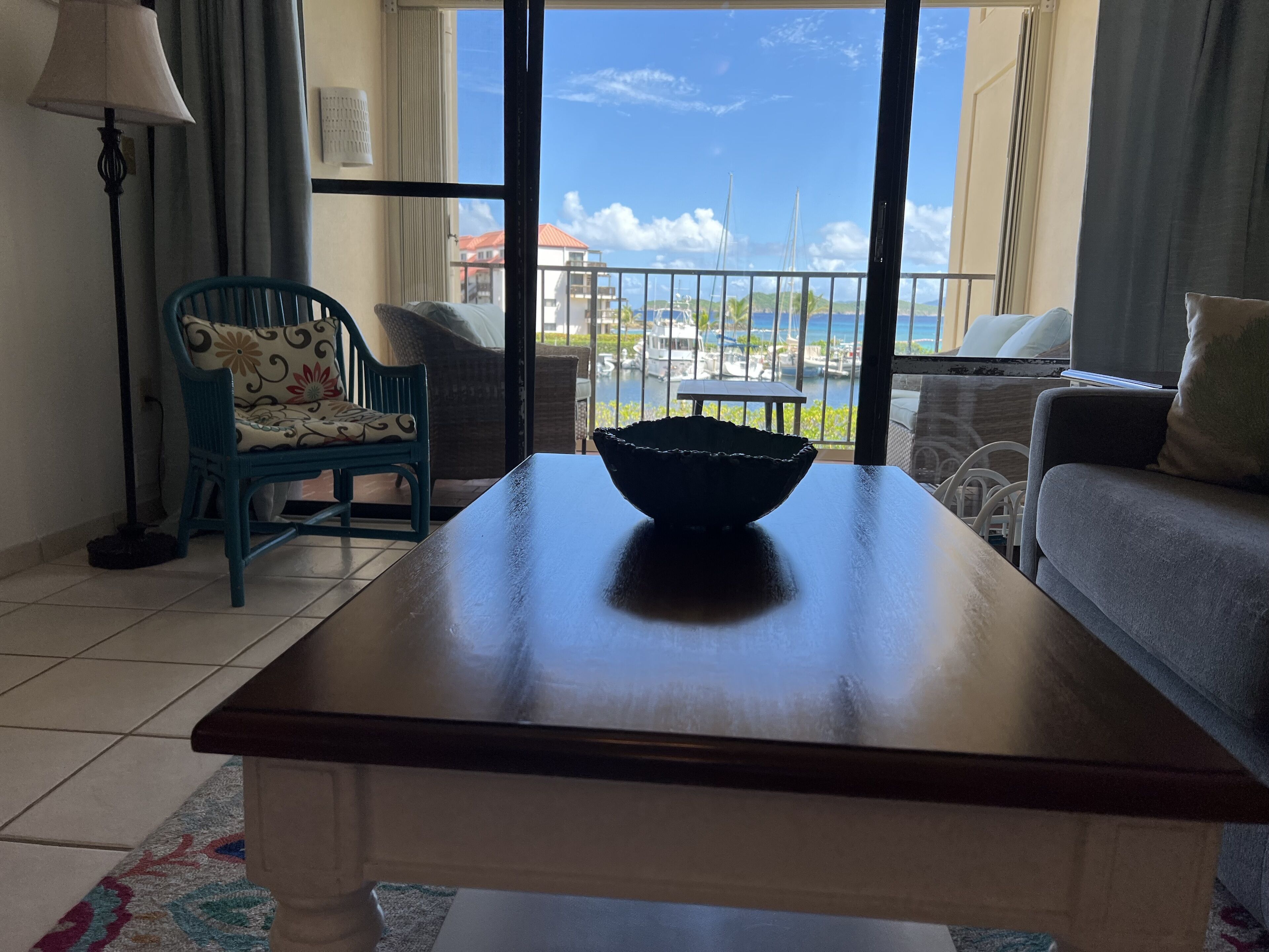 A room with a view of the marina, a wooden table with a bowl, a blue chair, and a grey sofa.