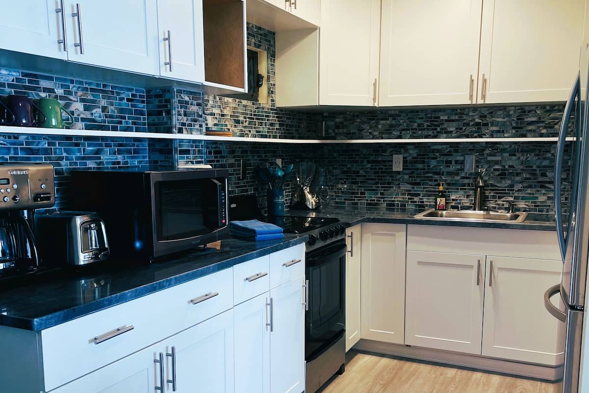 A modern kitchen with white cabinets, a black countertop, and a wooden floor.