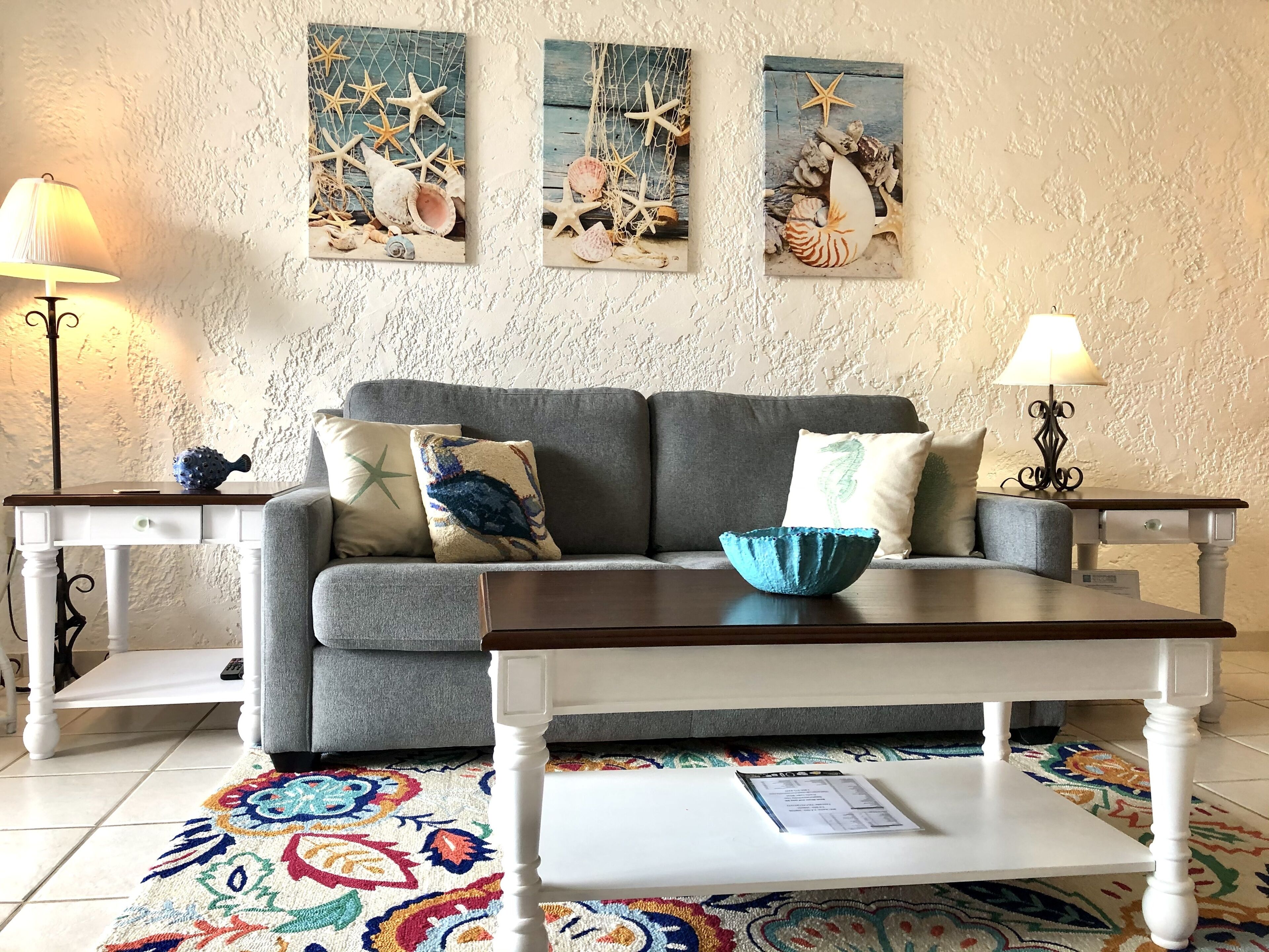 A living room with a grey sofa, two side tables, a coffee table, and a colorful rug.