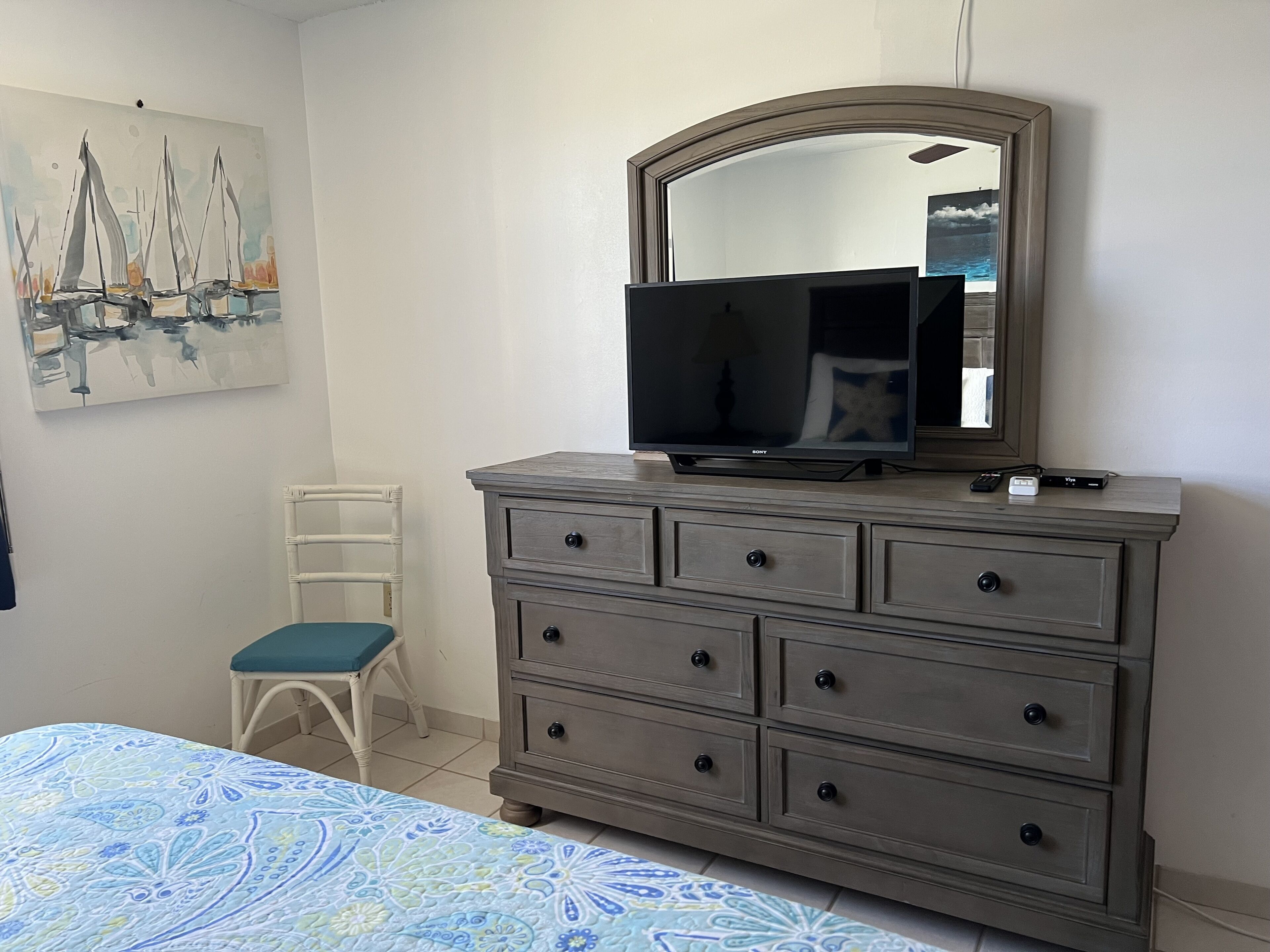 A bedroom with a bed, a dresser with a mirror, a chair, and a painting on the wall.