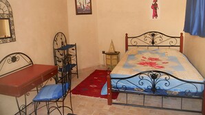 Ein Schlafzimmer mit Bett, Schreibtisch, Stuhl, einem kleinen Tisch und einem Wandregal.